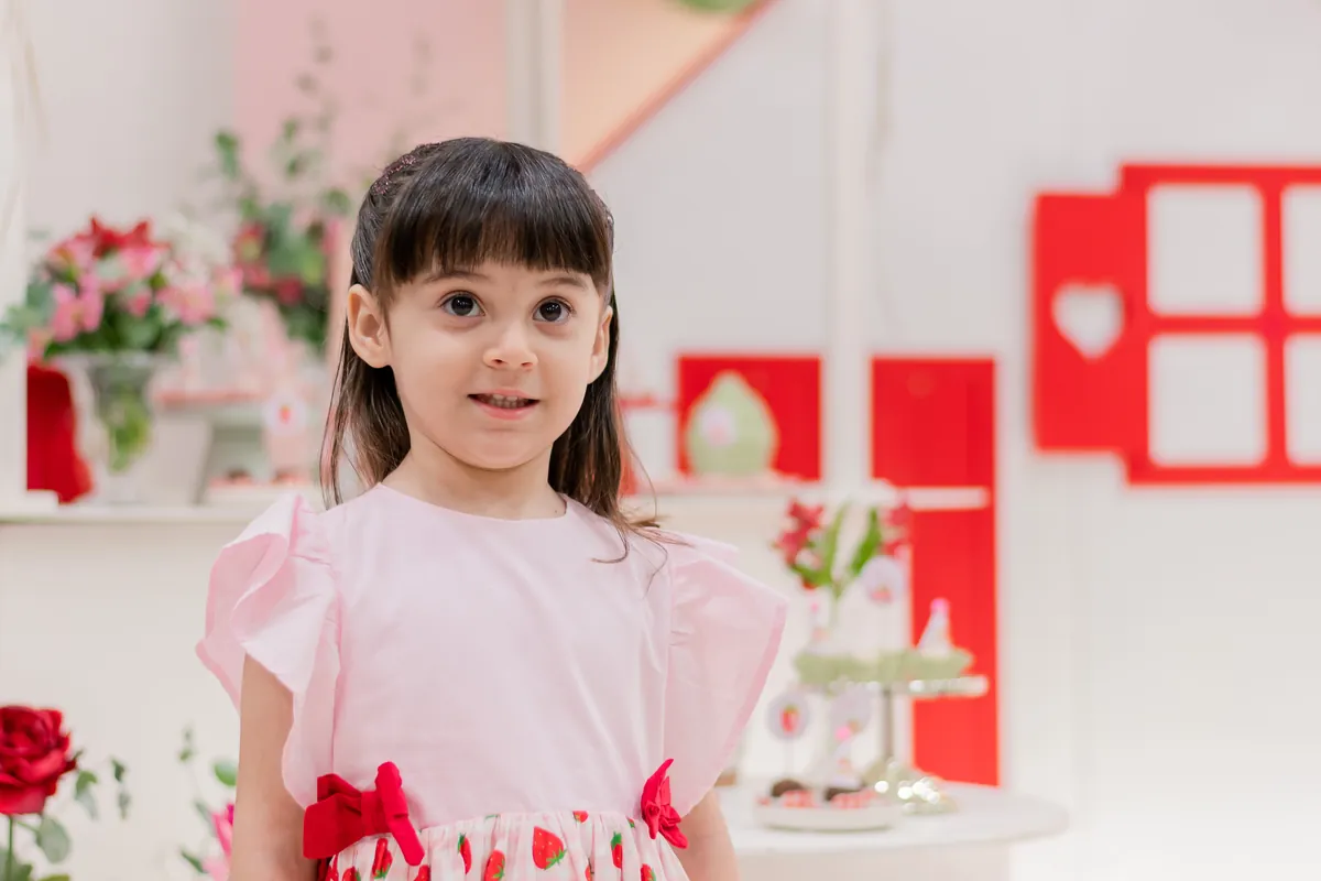 Menina em festa de aniversário infantil com decoração de morangos