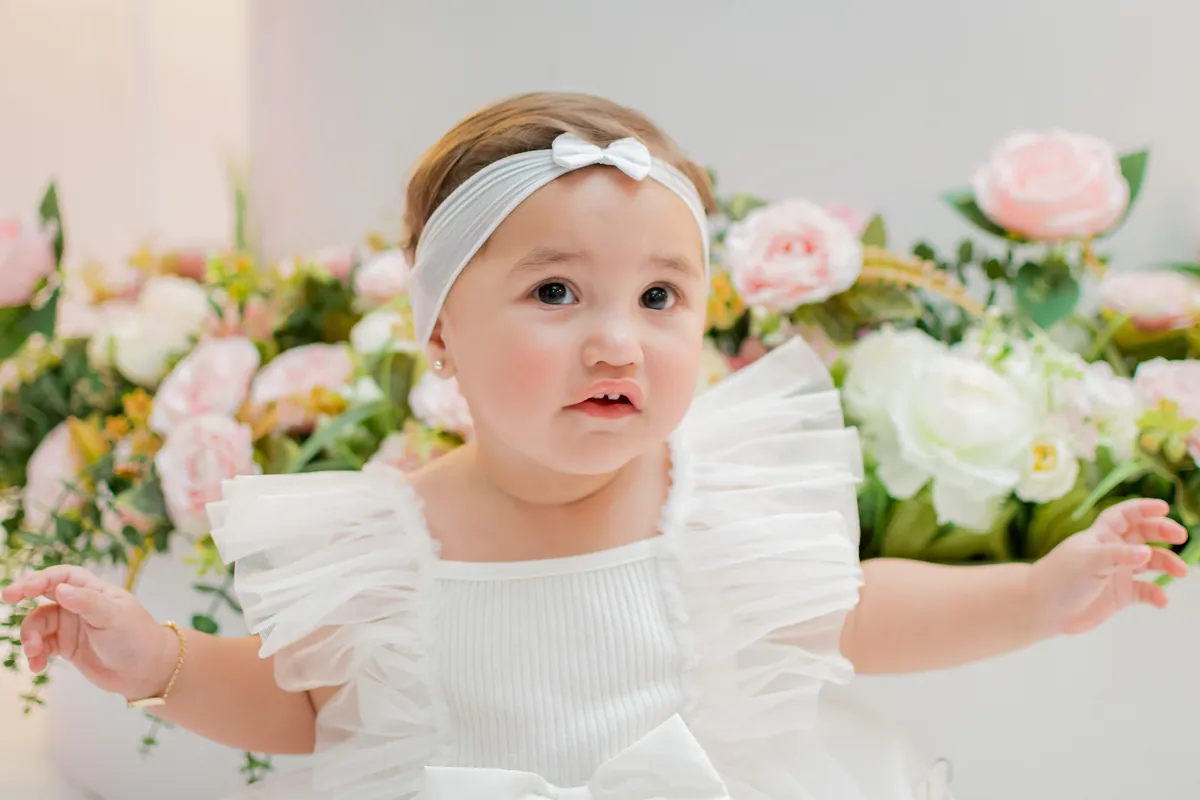 Bebê de vestido branco em festa de 1 ano com decoração floral em Londrina