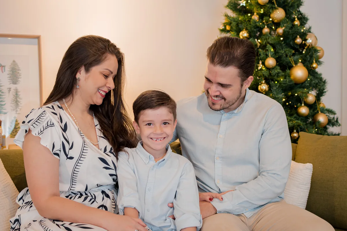 Pais e filho rindo no sofá em ensaio de Natal em Londrina