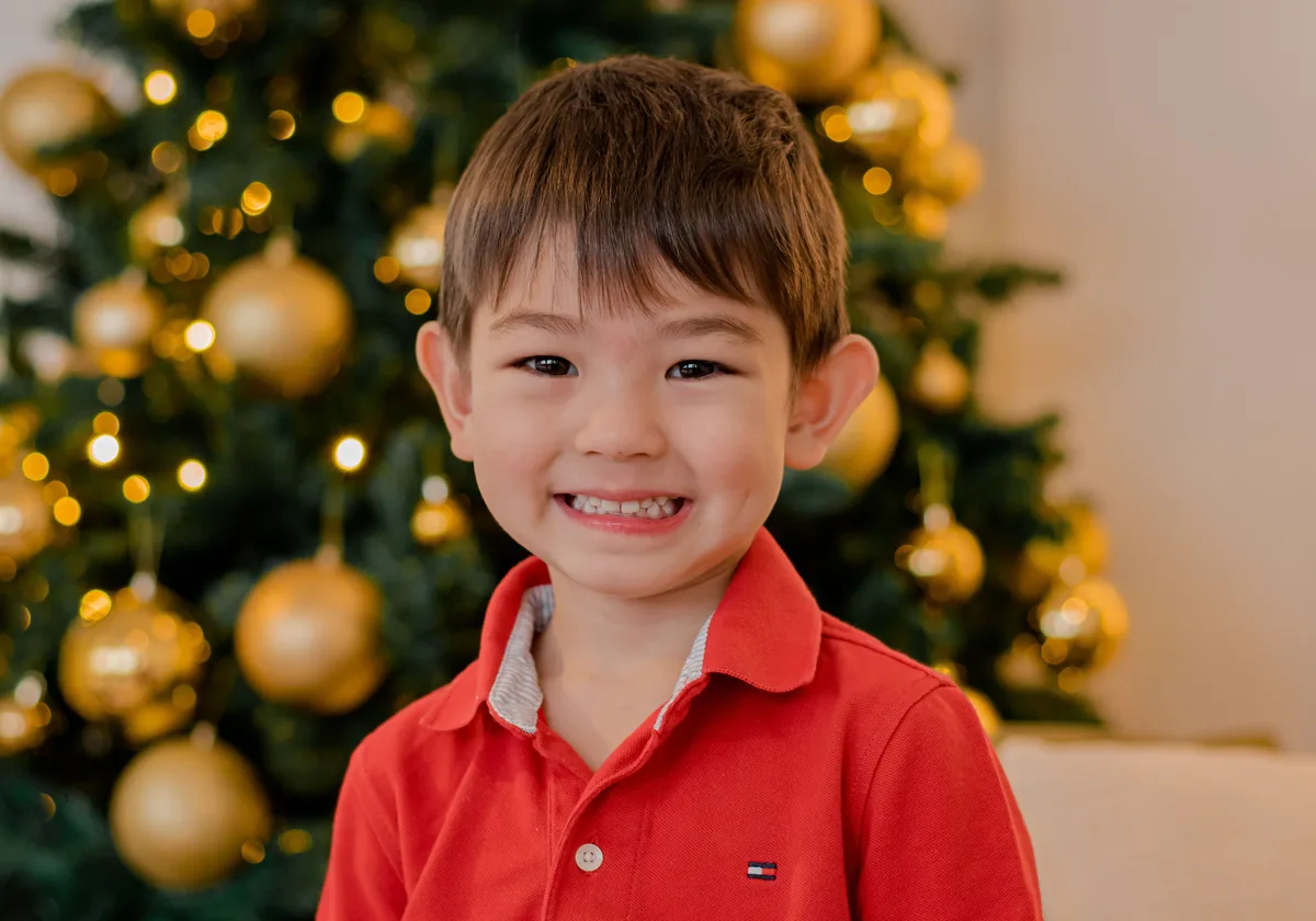 Menino de camisa polo vermelha em close com árvore de Natal desfocada